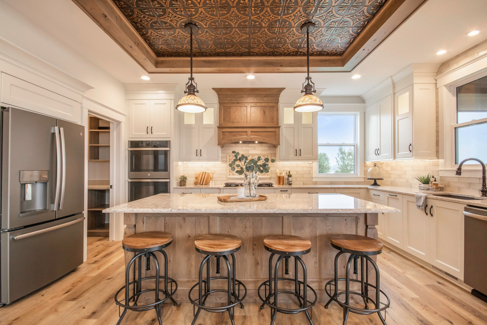 Inspiration for a transitional kitchen in Grand Rapids with an undermount sink, shaker cabinets, white cabinets, quartz benchtops, white splashback, stone tile splashback, stainless steel appliances, vinyl floors, with island, white benchtop and brown floor.