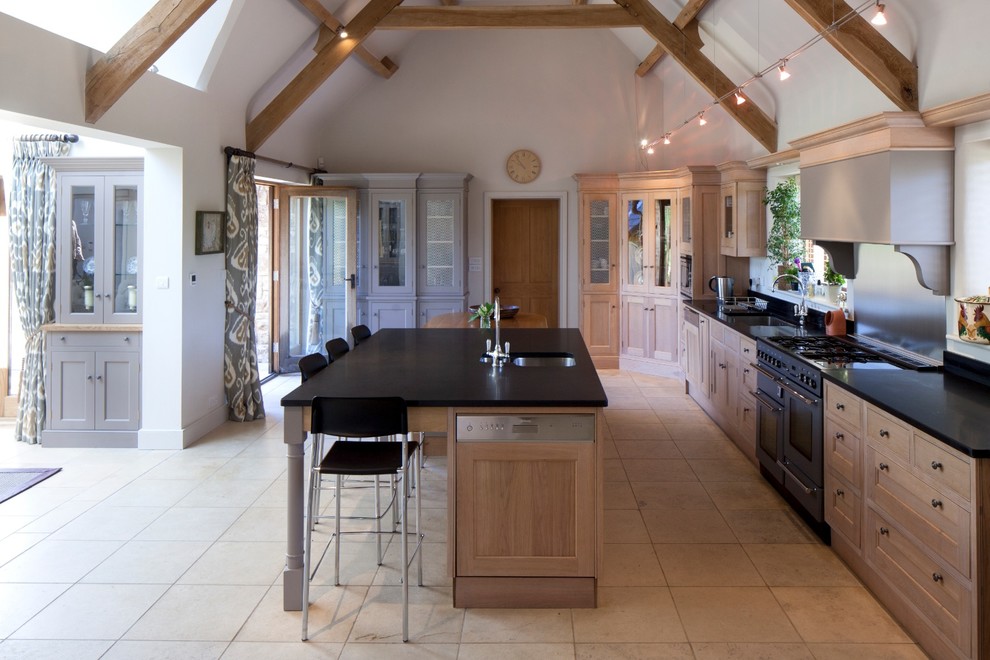 Photo of a country l-shaped eat-in kitchen in Gloucestershire with an undermount sink, beaded inset cabinets, medium wood cabinets, solid surface benchtops, metal splashback, coloured appliances, with island and metallic splashback.