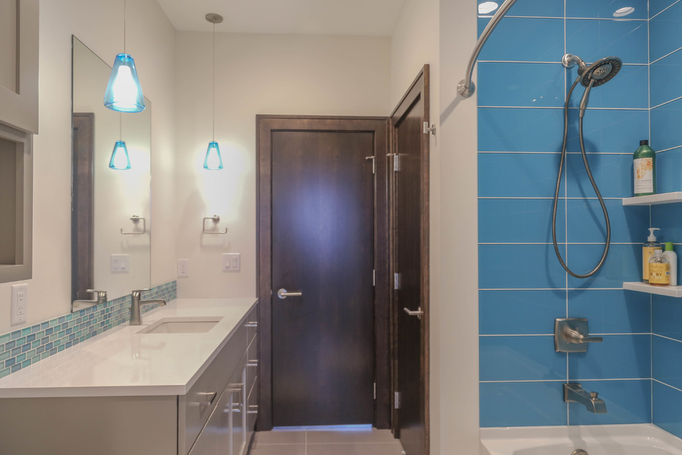 Example of a mid-sized transitional kids' gray tile and porcelain tile porcelain tile drop-in bathtub design with flat-panel cabinets, gray cabinets, a two-piece toilet, white walls, an undermount sink and quartzite countertops