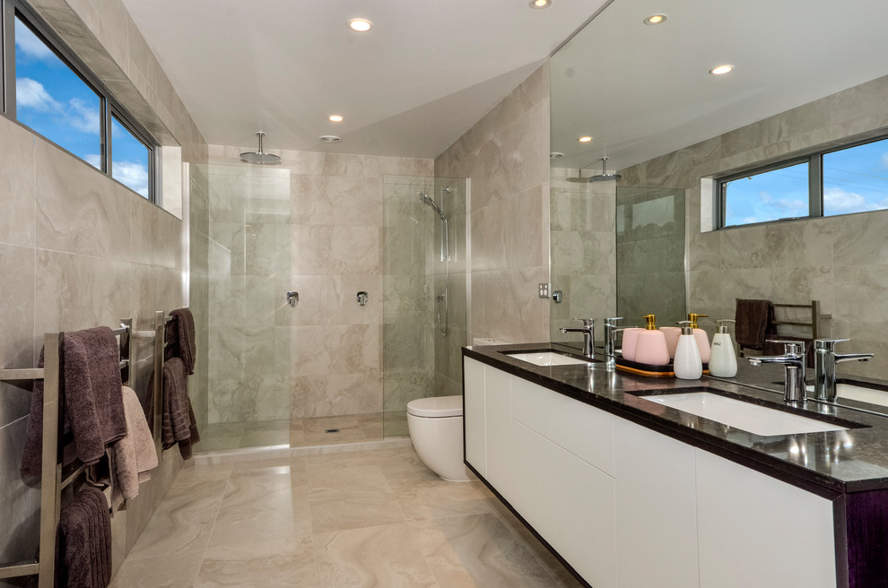 Inspiration for an expansive modern master wet room bathroom in Auckland with raised-panel cabinets, white cabinets, a one-piece toilet, beige tile, beige walls, a drop-in sink, beige floor, an open shower and black benchtops.