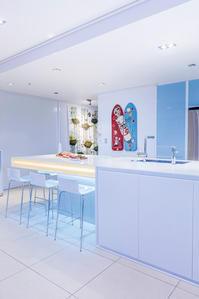 Inspiration for a large contemporary l-shaped eat-in kitchen in Auckland with a double-bowl sink, glass-front cabinets, blue cabinets, solid surface benchtops, blue splashback, glass sheet splashback, stainless steel appliances, porcelain floors and with island.