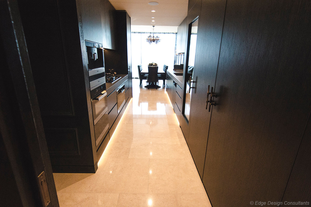 Large modern galley kitchen pantry in Sydney with an undermount sink, flat-panel cabinets, dark wood cabinets, tile benchtops, grey splashback, porcelain splashback, black appliances, porcelain floors, no island, beige floor and grey benchtop.