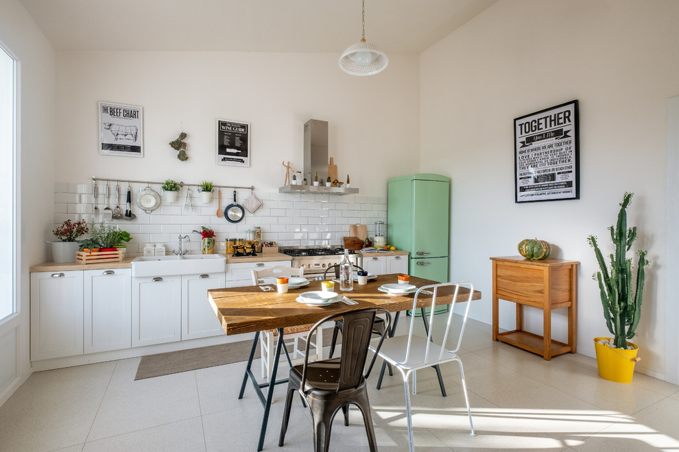 Photo of a mid-sized country single-wall eat-in kitchen in Bari with a farmhouse sink, shaker cabinets, white cabinets, wood benchtops, white splashback, subway tile splashback, coloured appliances, no island, grey floor and beige benchtop.