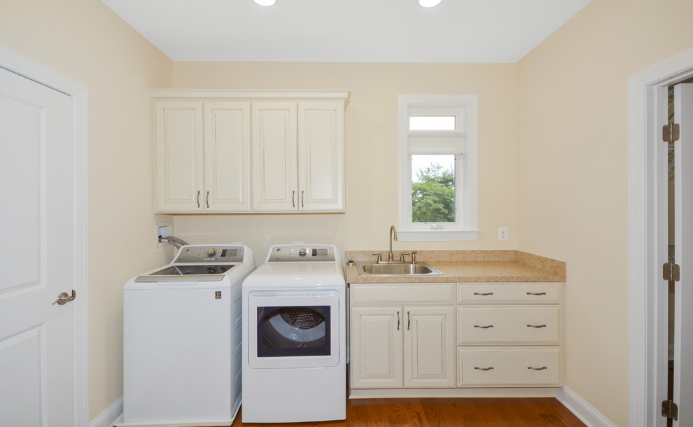 This is an example of a single-wall dedicated laundry room in DC Metro with a drop-in sink, raised-panel cabinets, white cabinets, laminate benchtops, medium hardwood floors and a side-by-side washer and dryer.