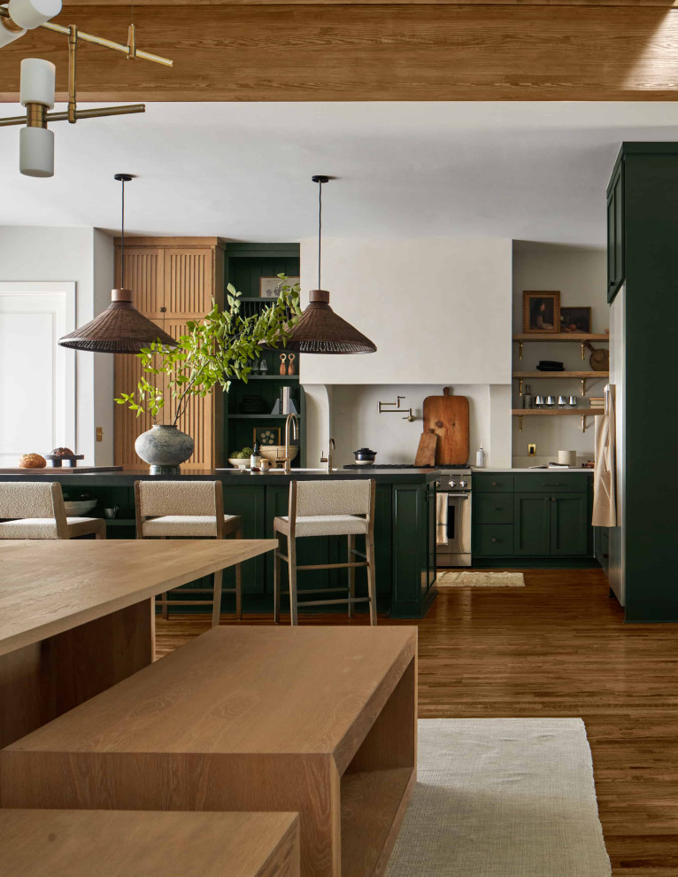 Diseño de cocina moderna grande con armarios estilo shaker, puertas de armario verdes, electrodomésticos de acero inoxidable, suelo de madera en tonos medios, una isla, salpicadero blanco y encimeras blancas