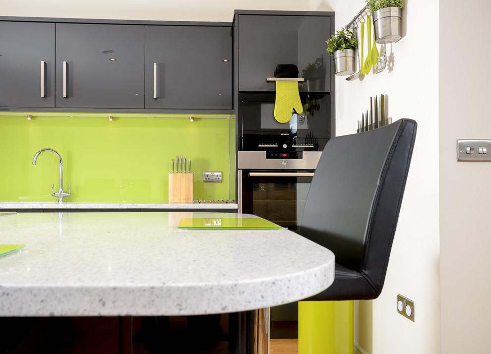Modern single-wall eat-in kitchen in Other with a drop-in sink, flat-panel cabinets, grey cabinets, solid surface benchtops, green splashback, glass sheet splashback, panelled appliances, vinyl floors and with island.