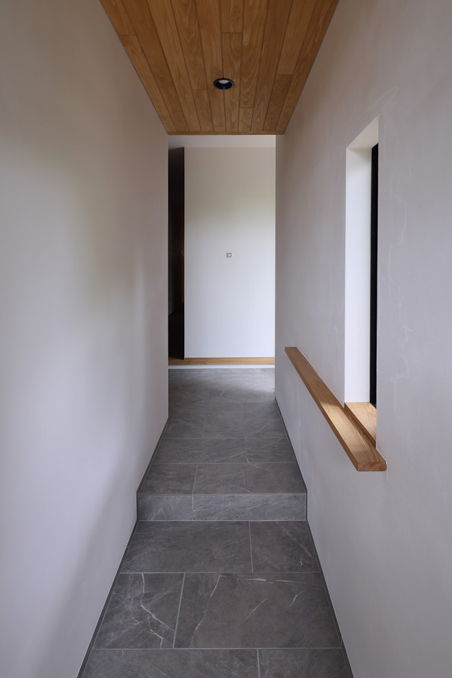 Idée de décoration pour un couloir nordique de taille moyenne avec un mur blanc, un sol en carrelage de céramique, un sol gris et un plafond en lambris de bois.