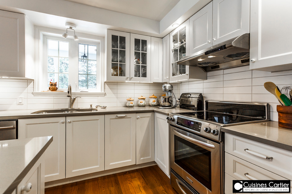Inspiration for a large transitional medium tone wood floor eat-in kitchen remodel in Montreal with a double-bowl sink, shaker cabinets, white cabinets, quartzite countertops, white backsplash, ceramic backsplash, stainless steel appliances and an island