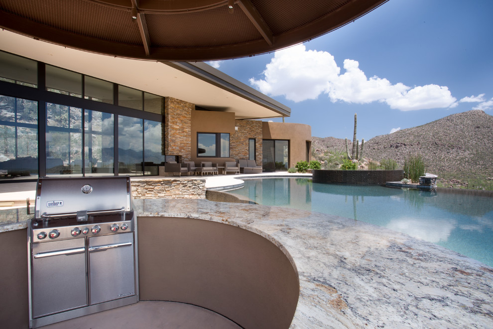 This is an example of a large contemporary backyard patio in Phoenix with an outdoor kitchen, natural stone pavers and an awning.