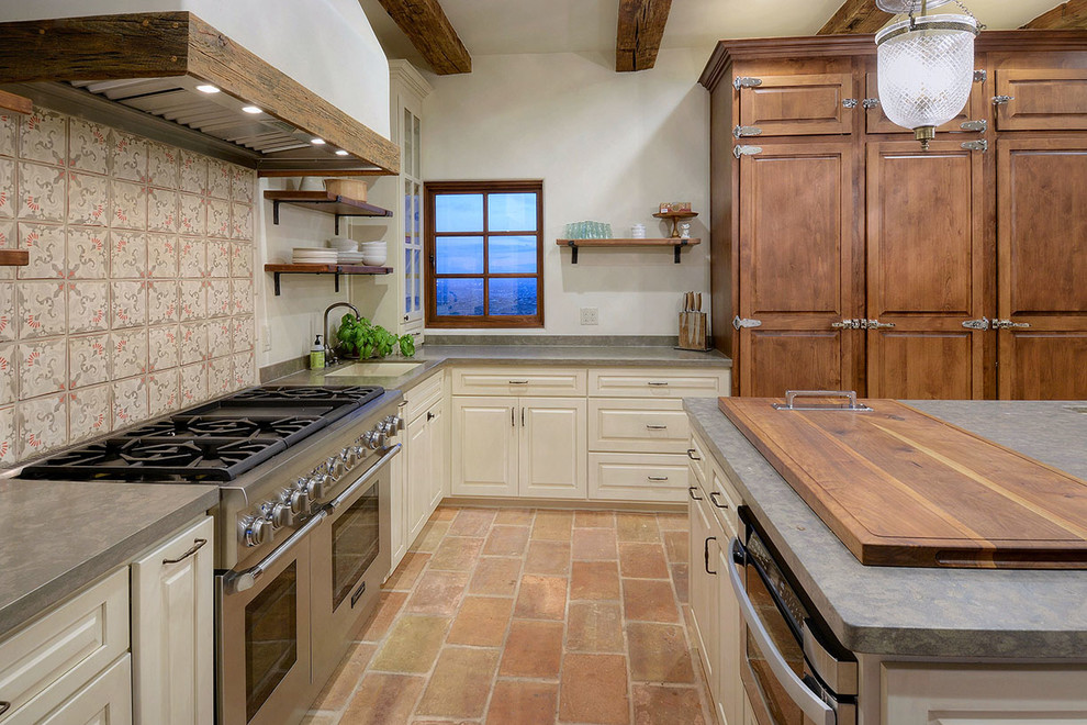 This is an example of a large mediterranean l-shaped separate kitchen in Other with a double-bowl sink, raised-panel cabinets, limestone benchtops, grey splashback, limestone splashback, stainless steel appliances, terra-cotta floors, with island and pink floor.