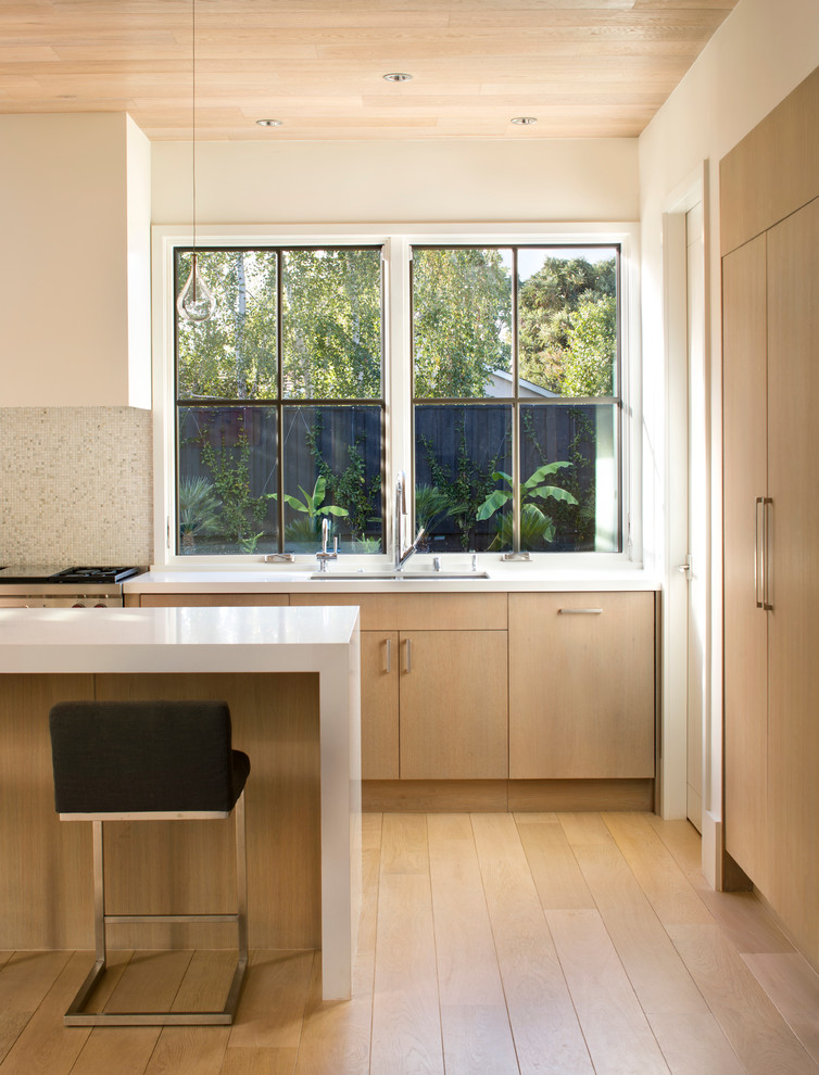Photo of a mid-sized contemporary single-wall open plan kitchen in San Francisco with a double-bowl sink, flat-panel cabinets, light wood cabinets, solid surface benchtops, stainless steel appliances, light hardwood floors and with island.