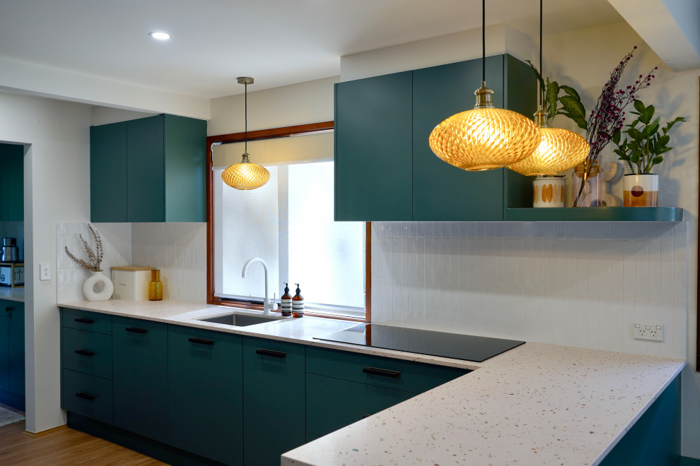 Design ideas for a large transitional galley open plan kitchen in Sydney with an undermount sink, flat-panel cabinets, green cabinets, terrazzo benchtops, white splashback, subway tile splashback, black appliances, light hardwood floors, with island, brown floor and multi-coloured benchtop.