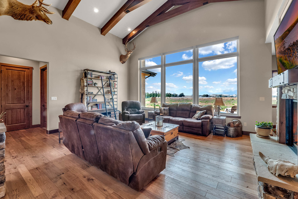 This is an example of a mid-sized country open concept living room in Denver with beige walls, medium hardwood floors, a two-sided fireplace, a stone fireplace surround and multi-coloured floor.