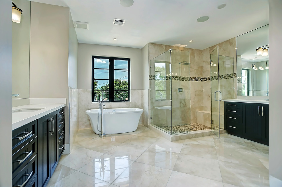 Design ideas for a large mediterranean master bathroom in Miami with furniture-like cabinets, black cabinets, a freestanding tub, a corner shower, beige tile, brown tile, pebble tile, beige walls, marble floors, an undermount sink, engineered quartz benchtops, beige floor and a hinged shower door.