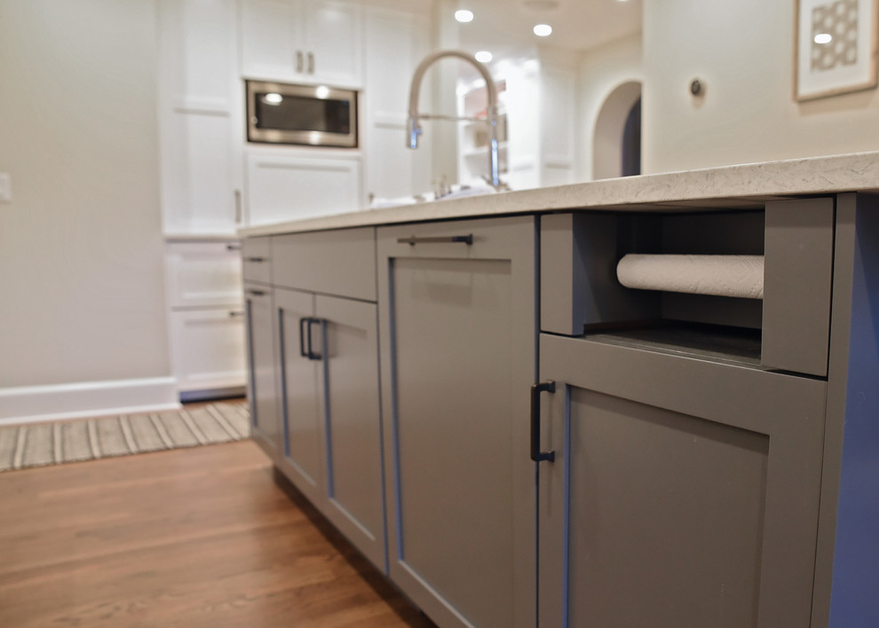 Inspiration for a mid-sized transitional medium tone wood floor and brown floor enclosed kitchen remodel with an undermount sink, flat-panel cabinets, gray cabinets, quartz countertops, white backsplash, ceramic backsplash, stainless steel appliances, an island and gray countertops