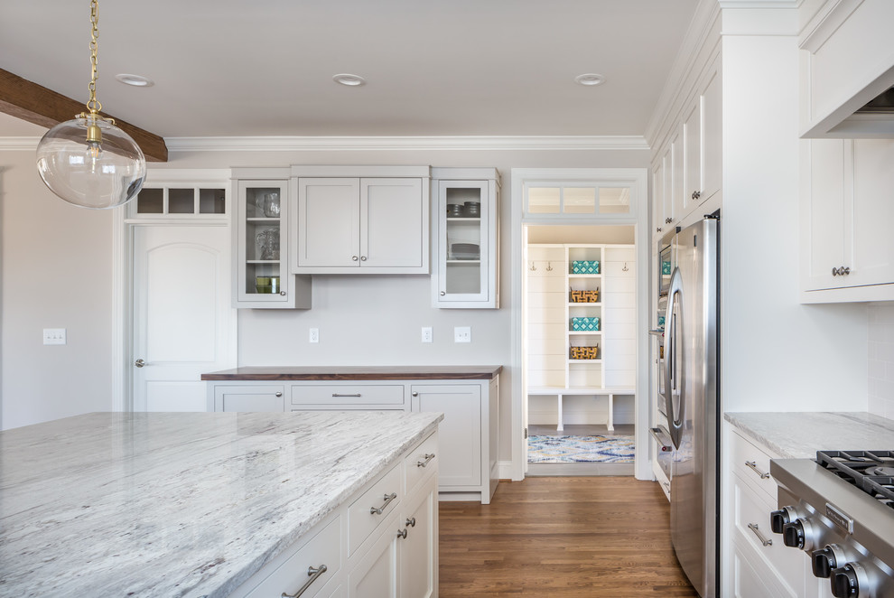 Large transitional u-shaped eat-in kitchen in Raleigh with a farmhouse sink, shaker cabinets, white cabinets, white splashback, stainless steel appliances, medium hardwood floors, with island, brown floor, quartzite benchtops, subway tile splashback and white benchtop.