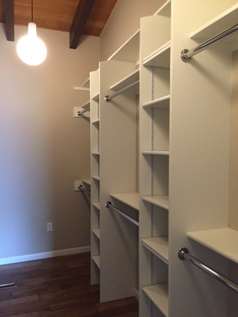 Photo of a mid-sized midcentury gender-neutral walk-in wardrobe in Cedar Rapids with white cabinets, open cabinets and dark hardwood floors.