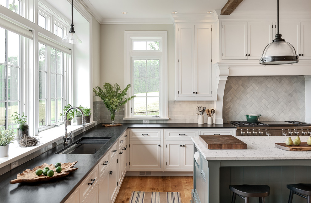 Example of a large classic l-shaped light wood floor, beige floor and exposed beam eat-in kitchen design in Bridgeport with an undermount sink, flat-panel cabinets, white cabinets, granite countertops, gray backsplash, ceramic backsplash, stainless steel appliances, an island and black countertops
