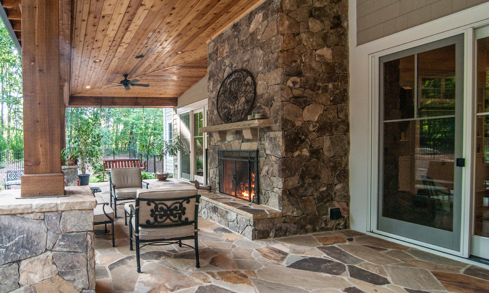 Réalisation d'un grand porche d'entrée de maison arrière tradition avec un foyer extérieur, des pavés en pierre naturelle et une extension de toiture.