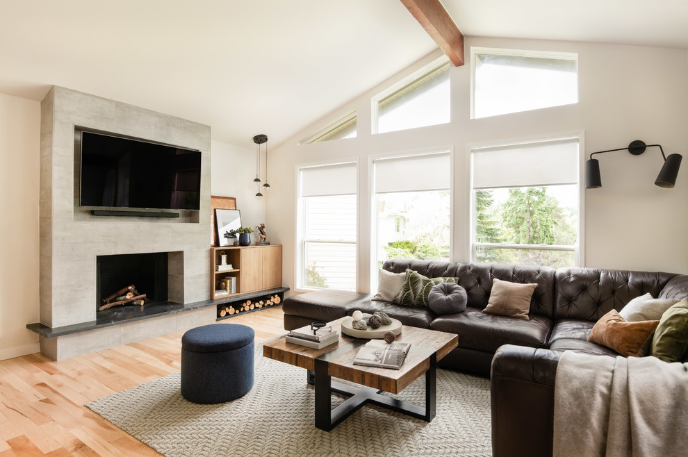 Photo of a mid-sized contemporary open concept living room in Seattle with white walls, light hardwood floors, a standard fireplace, a wall-mounted tv, beige floor and a concrete fireplace surround.