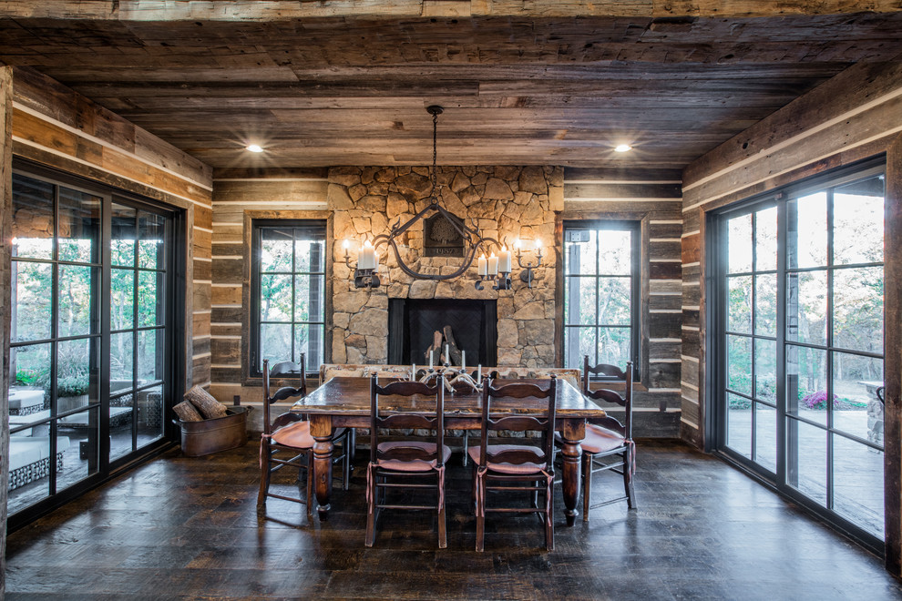 Inspiration for a country dining room in Austin with brown walls, dark hardwood floors, a standard fireplace, a stone fireplace surround and brown floor.