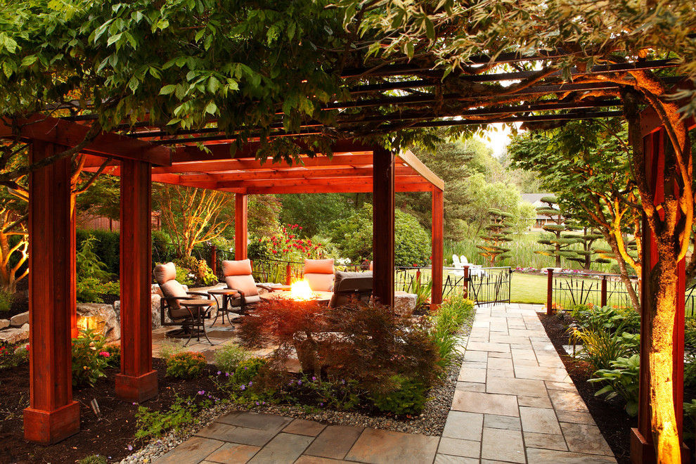 This is an example of a traditional backyard patio in Seattle with a fire feature, natural stone pavers and a pergola.