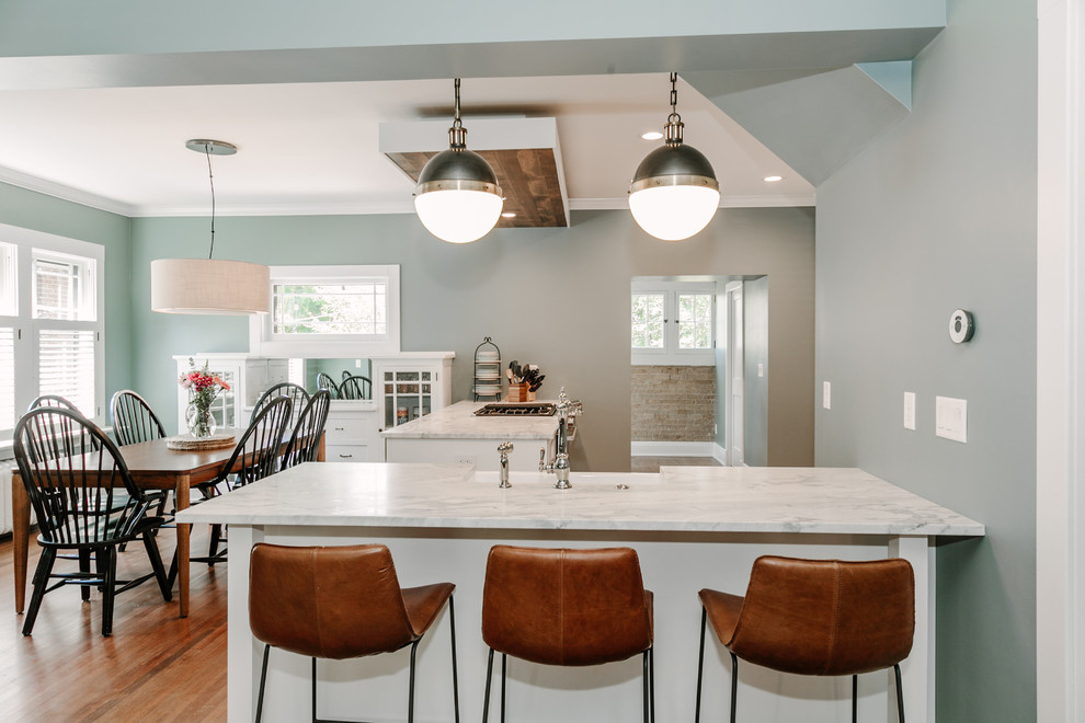 Design ideas for a mid-sized arts and crafts u-shaped eat-in kitchen in Denver with a farmhouse sink, shaker cabinets, white cabinets, solid surface benchtops, stainless steel appliances and dark hardwood floors.