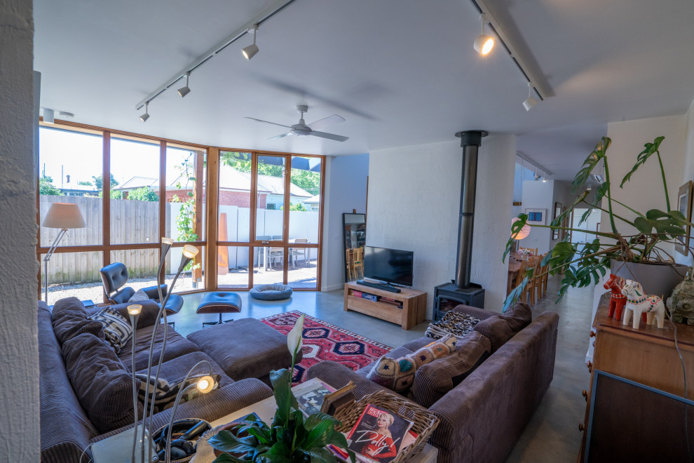 Mittelgroßes Landhausstil Wohnzimmer mit weißer Wandfarbe, Betonboden, Kamin, freistehendem TV und grauem Boden in Sonstige