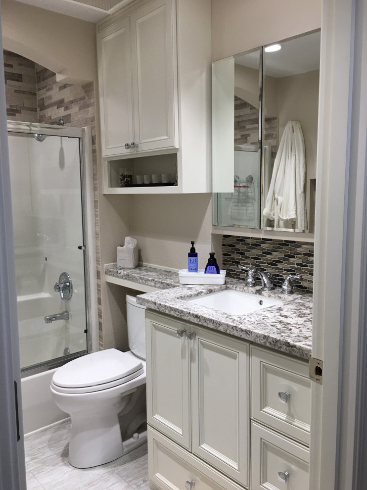Design ideas for a mid-sized traditional bathroom in Portland with raised-panel cabinets, white cabinets, an alcove tub, a shower/bathtub combo, a two-piece toilet, beige tile, stone tile, beige walls, linoleum floors, an undermount sink, granite benchtops, grey floor, a sliding shower screen, grey benchtops, a niche, a single vanity and a built-in vanity.