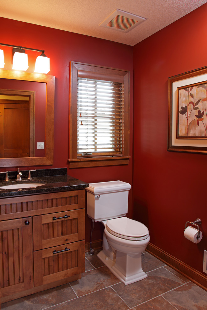 Inspiration for a traditional bathroom in Minneapolis with an undermount sink, medium wood cabinets, granite benchtops, multi-coloured tile, stone tile, red walls, limestone floors and recessed-panel cabinets.