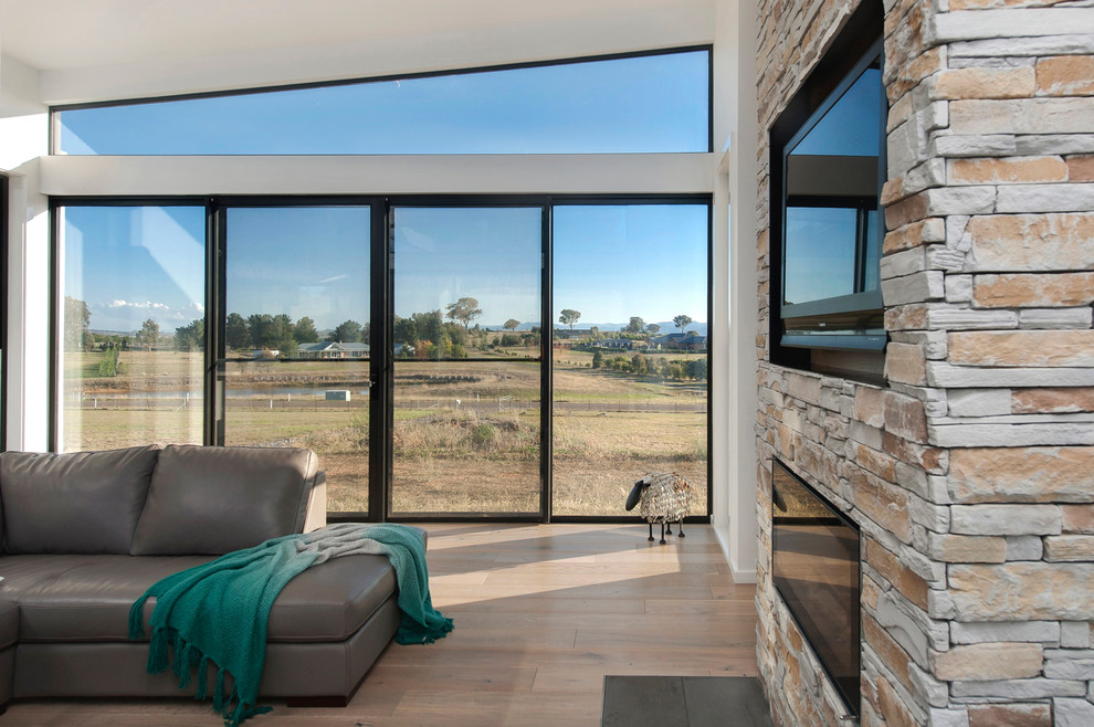Large contemporary open concept living room in Canberra - Queanbeyan with white walls, light hardwood floors, a standard fireplace, a stone fireplace surround and a wall-mounted tv.