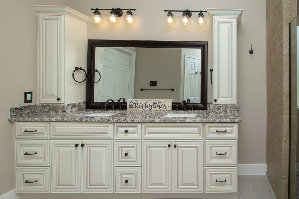 Large traditional master bathroom in Houston with raised-panel cabinets, white cabinets, a double shower, a one-piece toilet, beige tile, porcelain tile, beige walls, porcelain floors, an undermount sink, granite benchtops, grey floor, a hinged shower door and beige benchtops.