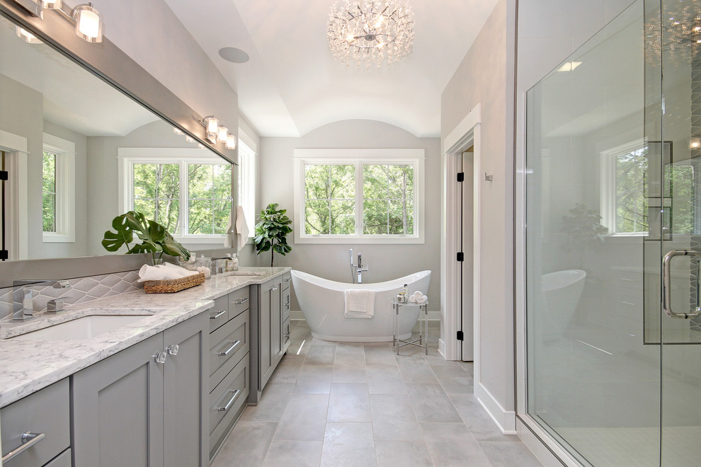 Design ideas for a transitional master bathroom in Grand Rapids with shaker cabinets, grey cabinets, a freestanding tub, an alcove shower, grey walls, an undermount sink, grey floor, a hinged shower door and white benchtops.