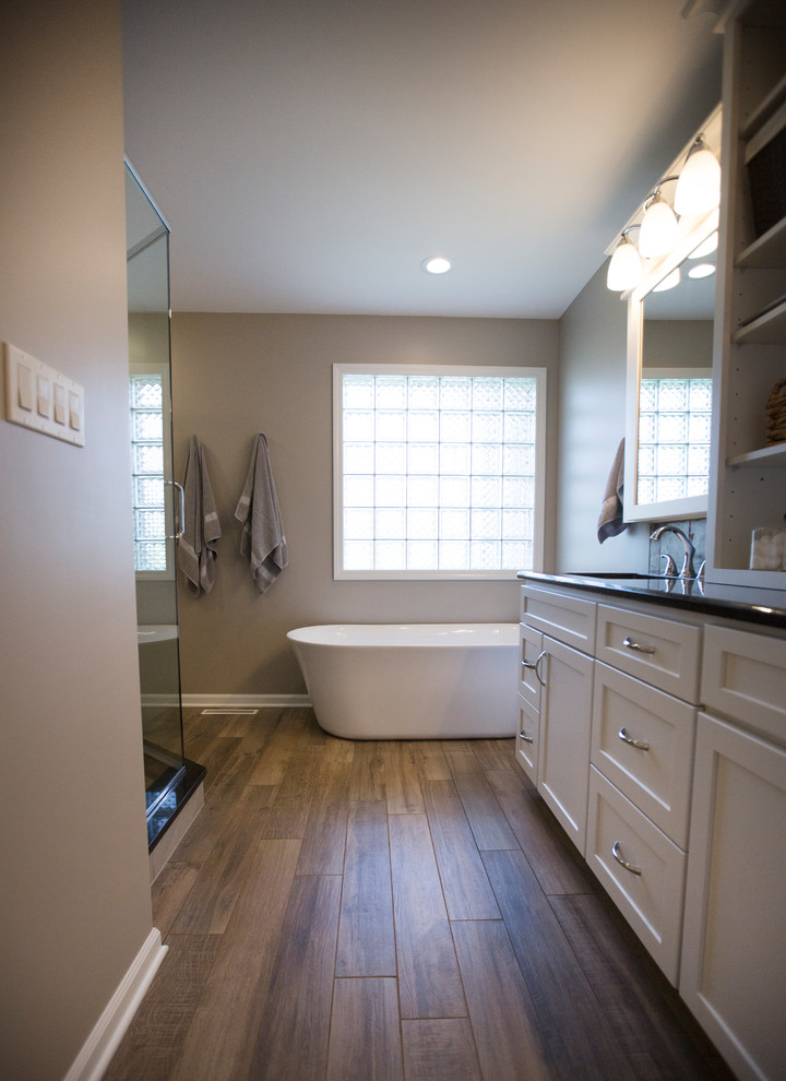 This is an example of a mid-sized transitional master bathroom in Chicago with flat-panel cabinets, white cabinets, a freestanding tub, porcelain floors, an undermount sink, granite benchtops, a corner shower, a two-piece toilet, beige tile, cement tile, beige walls, brown floor and a hinged shower door.