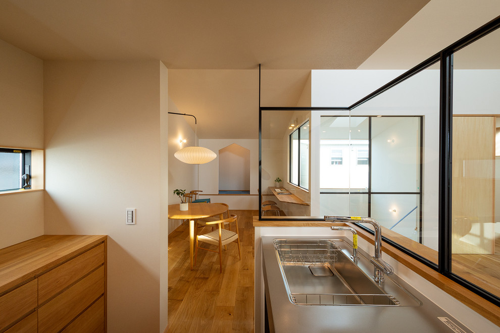 Minimalistisk inredning av ett kök, med en integrerad diskho, luckor med profilerade fronter, bänkskiva i rostfritt stål, vitt stänkskydd, linoleumgolv och beiget golv