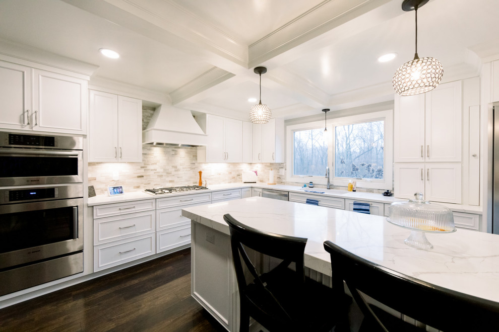 Photo of a large transitional kitchen in Cincinnati with white cabinets, quartz benchtops, beige splashback, marble splashback, vinyl floors, with island, brown floor, white benchtop and coffered.