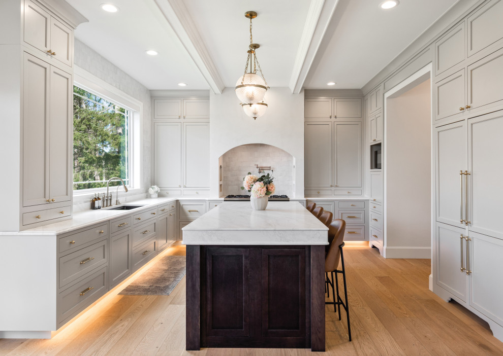 Kitchen - transitional u-shaped medium tone wood floor, brown floor and exposed beam kitchen idea in Seattle with an undermount sink, recessed-panel cabinets, gray cabinets, gray backsplash, paneled appliances, an island and white countertops