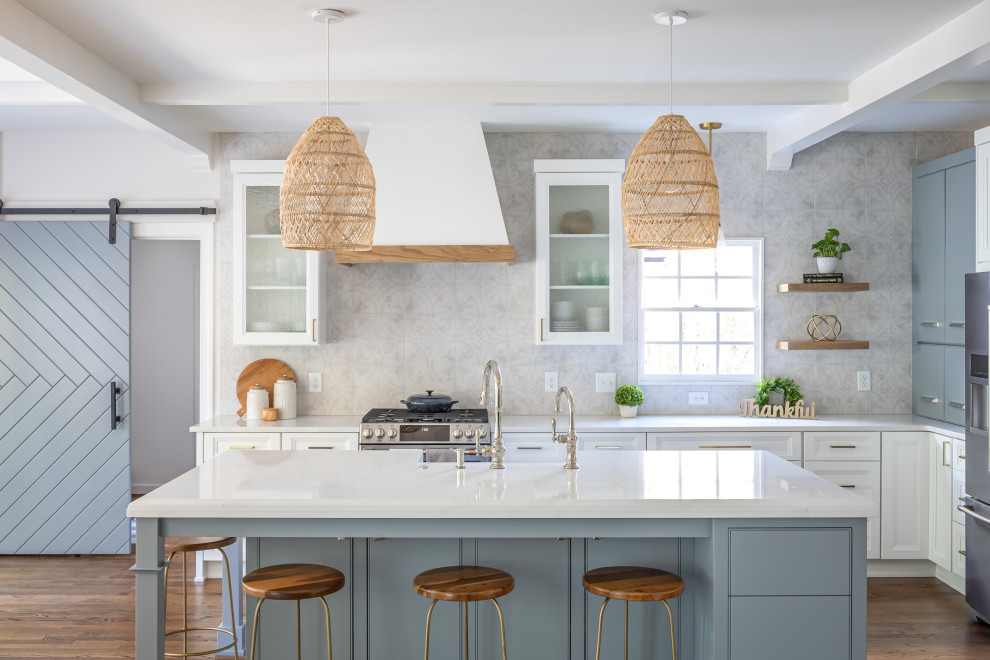 Inspiration for a mid-sized beach style l-shaped kitchen in Raleigh with recessed-panel cabinets, white cabinets, quartzite benchtops, porcelain splashback, stainless steel appliances, medium hardwood floors, with island, brown floor, white benchtop and grey splashback.
