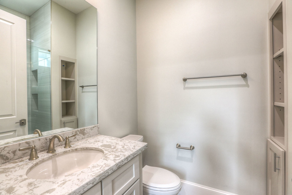 Mid-sized transitional 3/4 corner shower photo in Houston with shaker cabinets, an undermount sink, a hinged shower door, gray cabinets, a one-piece toilet and quartz countertops