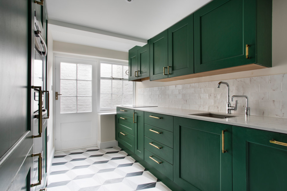 Design ideas for a small contemporary galley separate kitchen in London with a drop-in sink, shaker cabinets, green cabinets, solid surface benchtops, white splashback, porcelain splashback, stainless steel appliances, porcelain floors, grey floor and white benchtop.