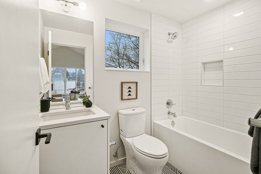 Design ideas for a medium sized scandinavian family bathroom in Seattle with flat-panel cabinets, white cabinets, a corner bath, a shower/bath combination, a two-piece toilet, white tiles, ceramic tiles, white walls, ceramic flooring, a submerged sink, engineered stone worktops, multi-coloured floors, a shower curtain, white worktops, a single sink and a built in vanity unit.
