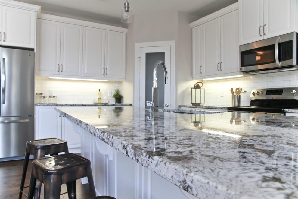Mid-sized transitional l-shaped dark wood floor and brown floor eat-in kitchen photo in Toronto with an undermount sink, raised-panel cabinets, white cabinets, granite countertops, white backsplash, subway tile backsplash, stainless steel appliances and an island