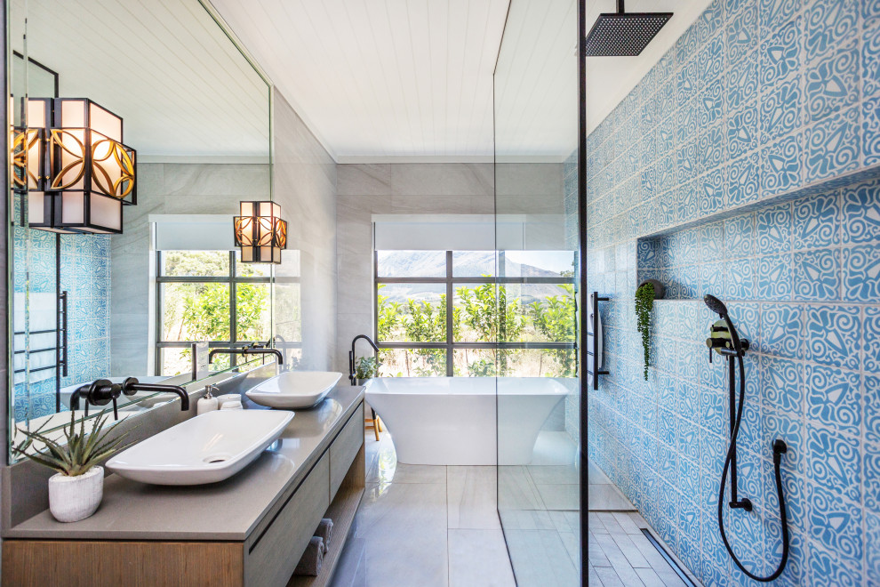 Contemporary bathroom in Melbourne with flat-panel cabinets, medium wood cabinets, a freestanding tub, blue tile, a vessel sink, grey floor and grey benchtops.