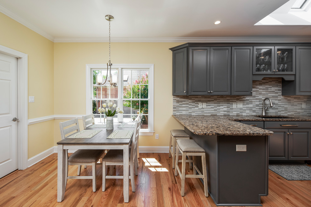 Example of a transitional kitchen design with raised-panel cabinets, gray cabinets, granite countertops, black appliances, a peninsula and multicolored countertops