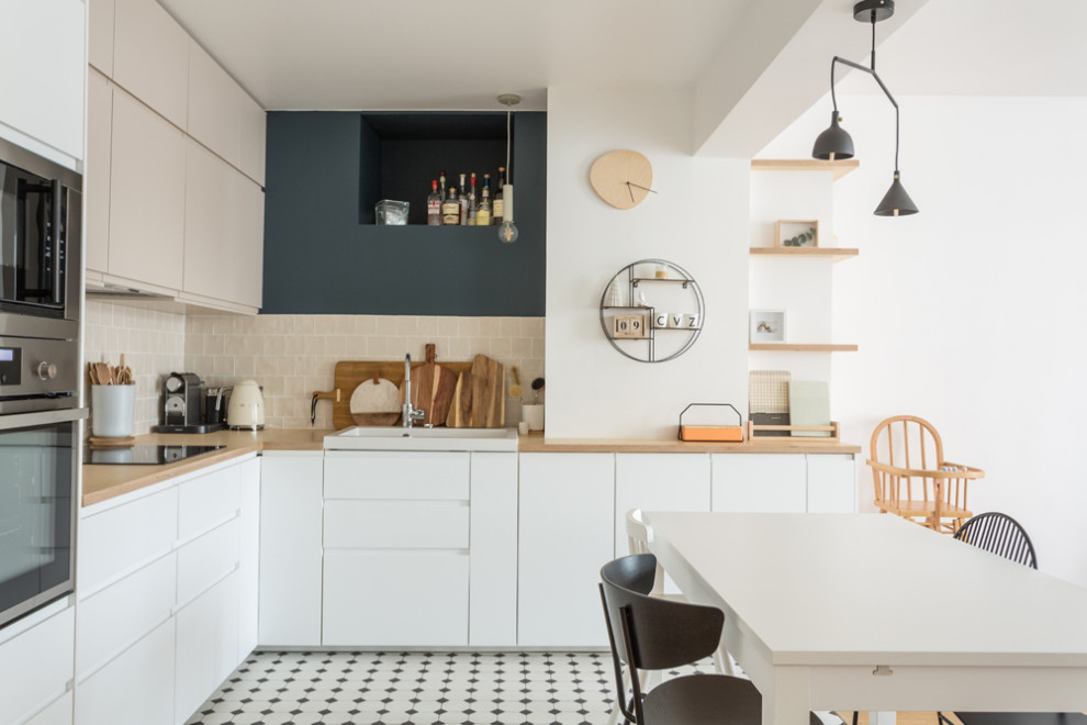 This is an example of a large scandinavian l-shaped open plan kitchen in Paris with a single-bowl sink, beaded inset cabinets, white cabinets, wood benchtops, beige splashback, terra-cotta splashback, stainless steel appliances, porcelain floors, no island, multi-coloured floor and beige benchtop.