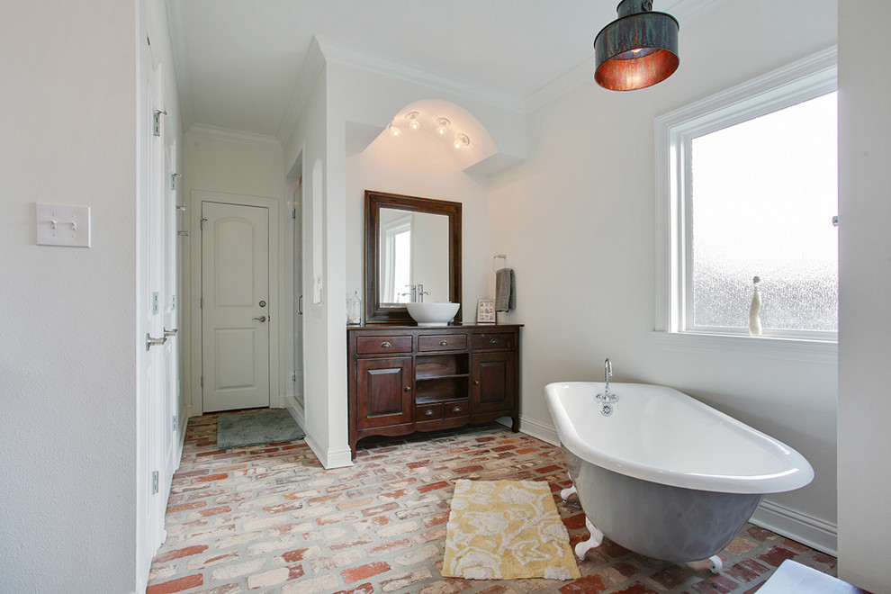 Inspiration for a large traditional master bathroom in New Orleans with a vessel sink, furniture-like cabinets, dark wood cabinets, wood benchtops, a freestanding tub, white walls and brick floors.