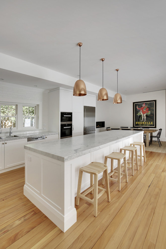 Inspiration for a large traditional l-shaped eat-in kitchen in Sydney with a double-bowl sink, shaker cabinets, white cabinets, marble benchtops, white splashback, ceramic splashback, stainless steel appliances, light hardwood floors, with island and yellow floor.