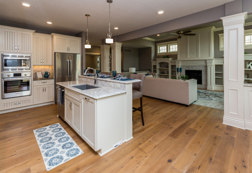 Inspiration for a transitional l-shaped kitchen pantry remodel with an undermount sink, beaded inset cabinets, white cabinets, quartz countertops, beige backsplash, stone tile backsplash, stainless steel appliances and an island