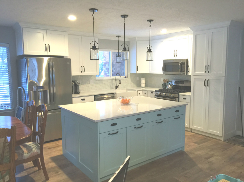 This is an example of a large modern l-shaped kitchen pantry in Salt Lake City with with island, a farmhouse sink, recessed-panel cabinets, white cabinets, quartz benchtops, stainless steel appliances, light hardwood floors, white splashback, mosaic tile splashback, beige floor and white benchtop.