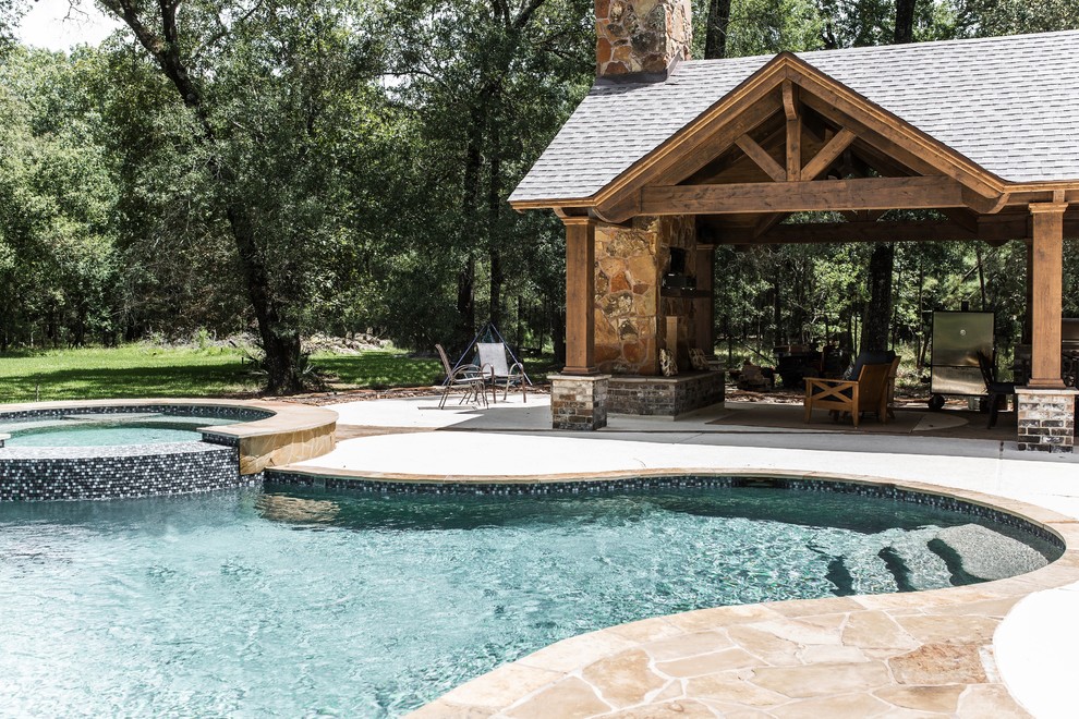 This is an example of a large country backyard custom-shaped pool in Houston with a hot tub and natural stone pavers.